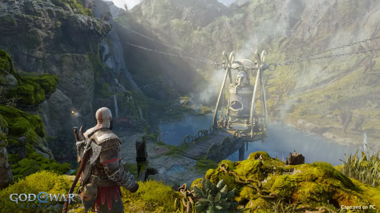 Kratos standing on a cliff overlooking a lush green valley with a structure in the distance